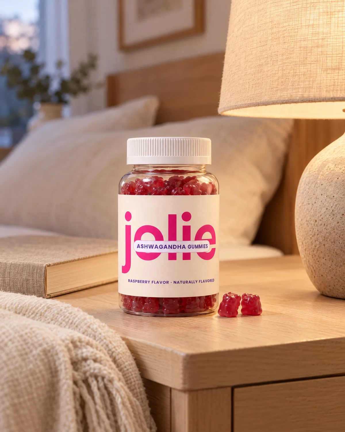 A jar of jolie Ashwagandha gummies on a bedside table next to a lamp and a book